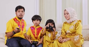 Happy muslim family playing video games together in living room while sitting on the sofa at home. Shot in 4k resolution during Ramadan Kareem