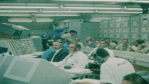 1960s: Control room. Men sit and talk. Men work on computer.