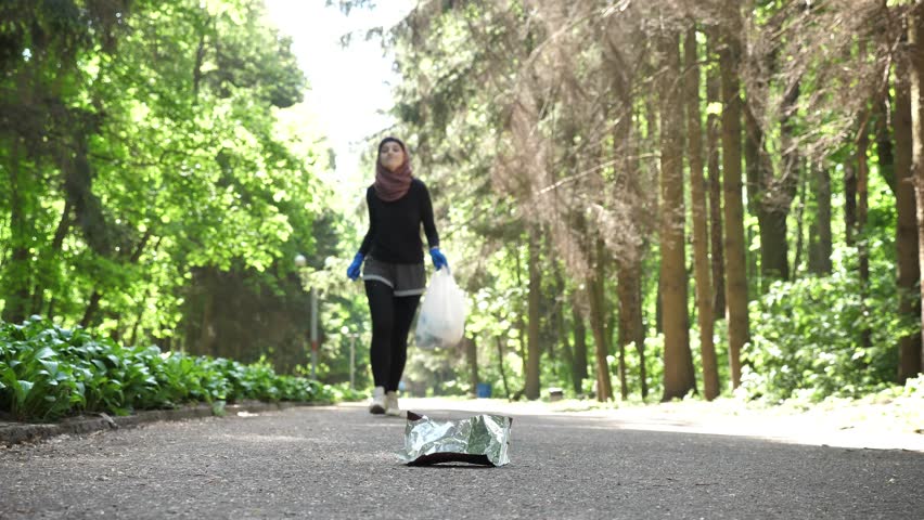 Plogging concept, young girl in hijab runs through park and cleans up garbage. 50 fps