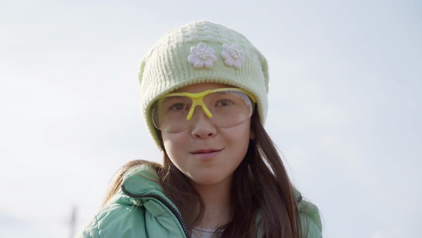 A girl waves a stick. a little girl in a green hat and glasses looks at the camera.