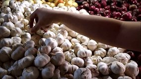Video of a person's hand picking from a pile of garlic at a vegetable store