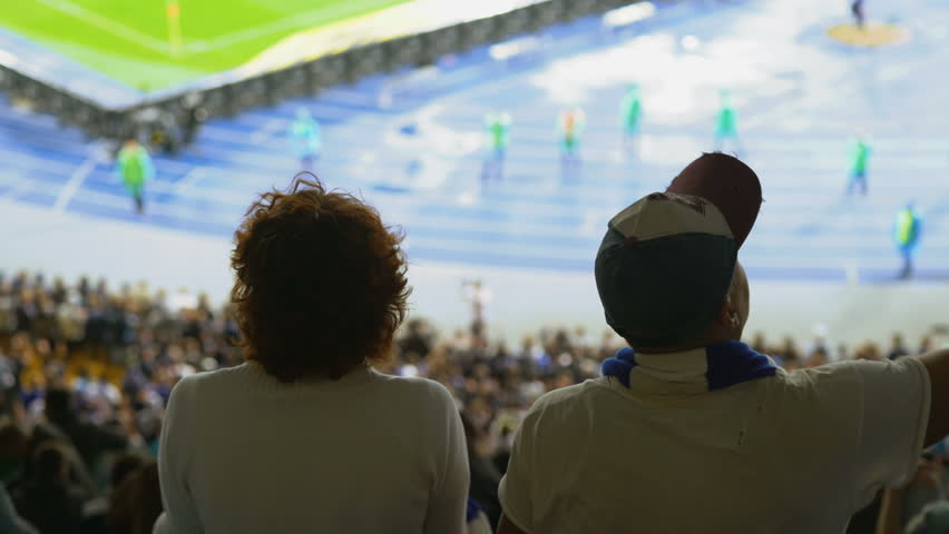 Middle-aged couple watching soccer game, clapping hands, waving team flag. Football fans supporting their team, 4K