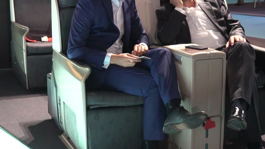 Business men using mobile phones in first class section of commercial airliner. Medium shot with camera dolly and focus on foreground passenger Royalty-Free Stock Footage #1010849528