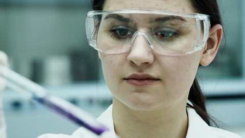 One caucasian beautiful laboratory assistant making clinical expertise, discovery molecular reaction in test-tube close up. Female person in protective safety mask holding pipet and dropping substance