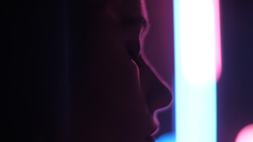 closeup side view young woman disappears slowly from camera in room with pink and blue blurred lamps Royalty-Free Stock Footage #1010857862