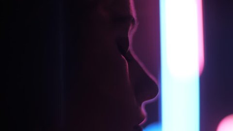 closeup side view young woman disappears slowly from camera in room with pink and blue blurred lamps