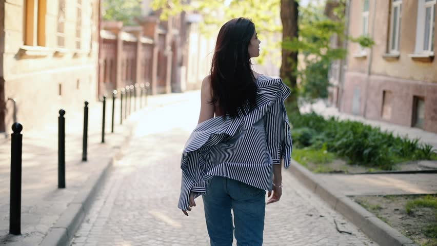 Attractive young woman walking in the city street and smile. Hair blowing in the wind