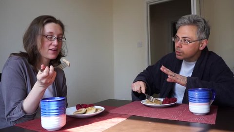 Couple (man and woman) having a disagreement while eating breakfast at a table.