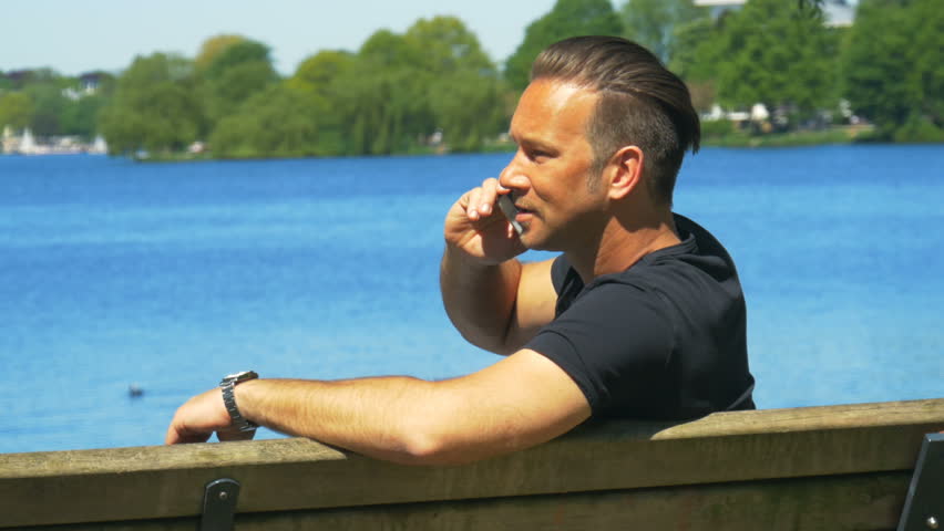 A man is talking on a mobile phone on a park bench