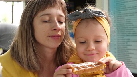 Cute woman and little child girl portrait while eating Belgian waffle, mother kiss daughter cheek
