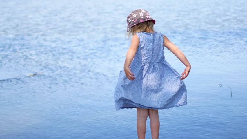 Young girl in dress standing with open arms at lakeside