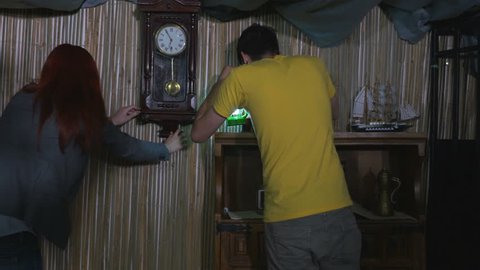 Man and woman finding a key in a wall clock and opening a cabinet in escape room game