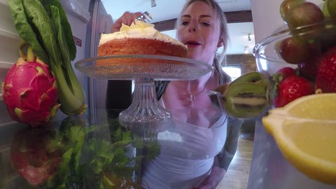 A 4K shot of a woman opening a fridge door and sneakily eating some cake without anyone knowing.