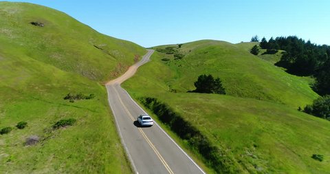 Aerial view of car driving down country road through rural grasy hills