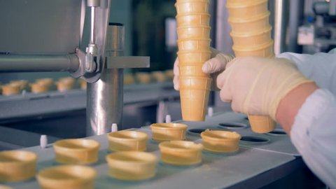 Factory worker is putting wafer cups into a moving conveyor belt