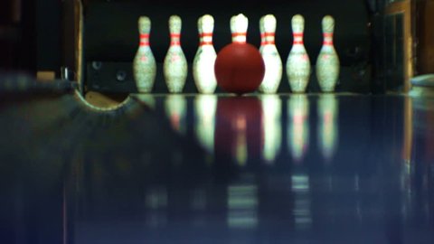 Bowling ball, rolling along a bowling alley, hits bowling pins and knocks out a strike.