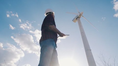 engineer at windmill power plant with tablet in hand on sky background