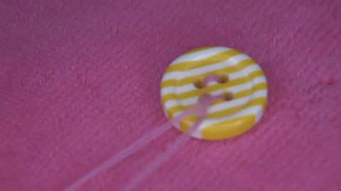 Sewing an colorful button on pink fabric, with pink thread, close up
