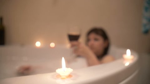 beautiful woman in a bath with foam and candles drinking wine