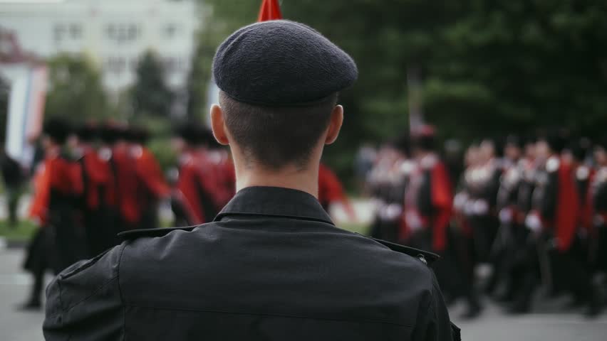 A column of military soldiers march against the background of a paratrooper in a beret