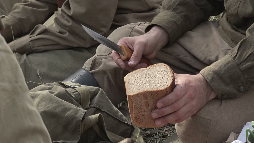 Close-up of soldiers in a Russian military uniform from the Second World War slices bread with a knife