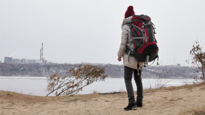 An attractive young woman in a red hat walks through the forest in early spring with a large tourist backpack 4 