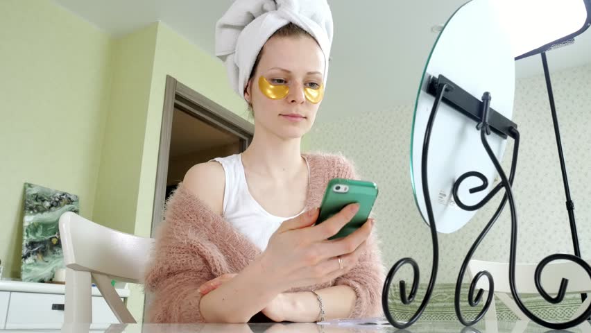 attractive business woman applying cosmetic facial spots at home, talking on the phone 4k