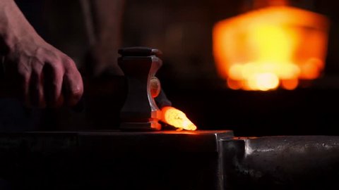 Get out of the furnace hot metal to make a sword war. Master of ancient art creates metal products. In slow motion blacksmiths hammer on red metal flying sparks.