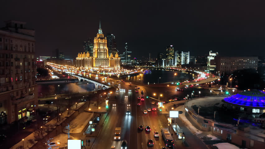 The illuminated Hotel surrounded by Moscow river. Intensive traffic on the city streets. Cityscape and the night lights on the New Arbat street.
