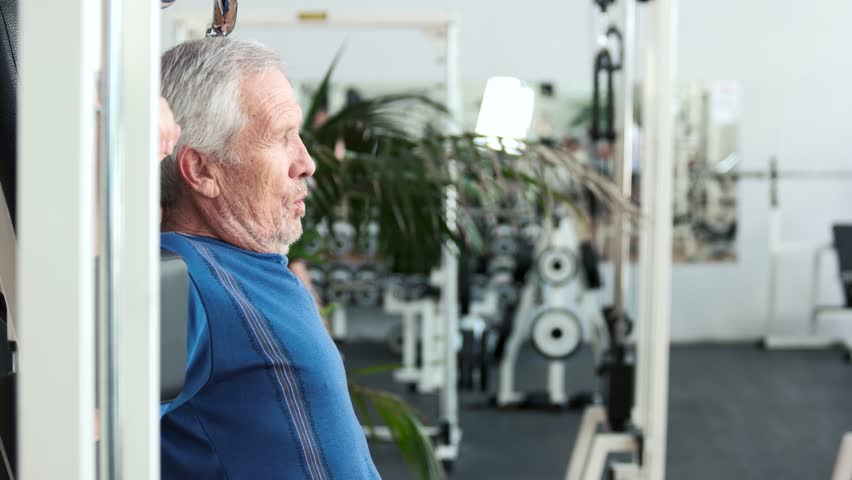 Elderly fitness athlete doing chest exercises. Senior man training at gym, side view.
