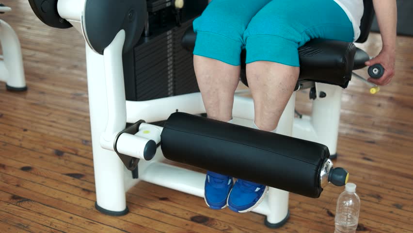 Close up female legs on weight lifting machine. Elderly woman doing weight lifting exercise at gym.