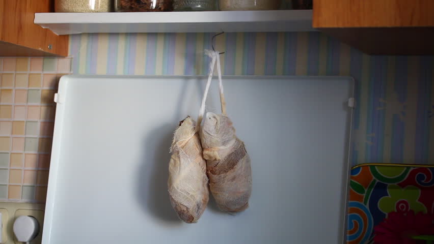The man takes off the chicken legs hung from the stove above the stove, wrapped in gauze. Preparation of dried chicken fillet.