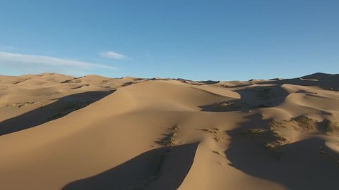 Beautiful aerial drone shot flying over sand dunes in Gobi desert. Located in Mongolia, blue sky sunny day. Low altitude flight.