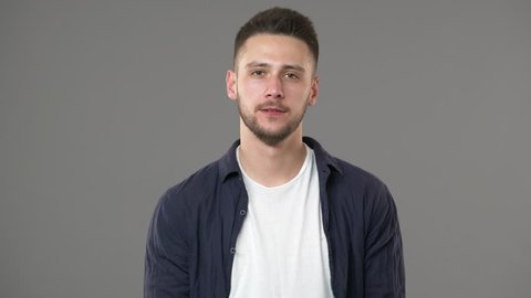 Portrait of good-looking guy in casual clothing posing with doubting look while thinking or weighing pros and cons, isolated over gray background. Concept of emotions