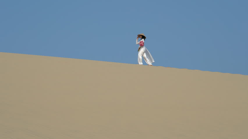 4K Movie of Beautiful Vietnamese holding Pink Lotus Walking on White Sand dune desert, Muine, Vietnam