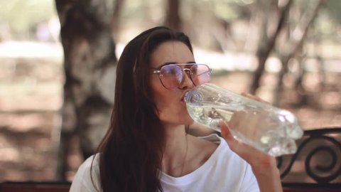 Young girl is drinking mineral water, Portrait of a young girl drinking water. Happy smiling young woman enjoying nature.