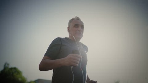 Senior seventy years old man jogging at sunset. Evening running
