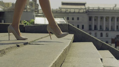 Perfect slim female legs in trendy high heel shoes stepping down on stairway in the city on sunny day over amazing urbanscape bacground. Elegant woman in high heels walking down staircase. Close-up.
