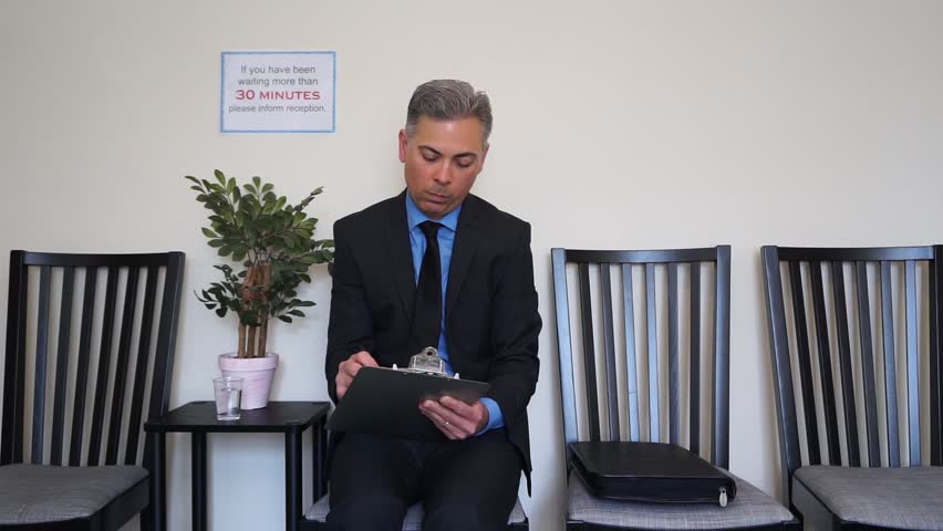 Man in waiting room concentrates as he fills out forms on a clipboard.