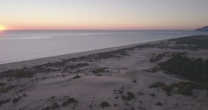 Aerial drone video orbiting left behind tall sand dune mountain viewpoing view of Turkey's longest sand beach, sun dipping into the sea over horizon at sunset in Patara, Turkey. 4k at 23.97fps