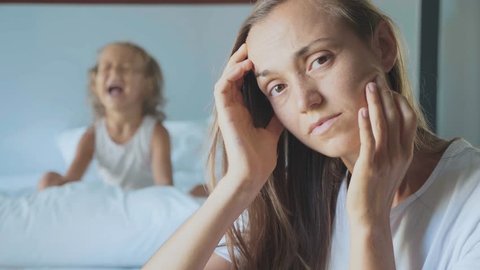 Portrait of upset tired mother with angry little child girl screaming and beating pillow on the background in slow motion. A hyperactive difficult kids and despairing parents concept.