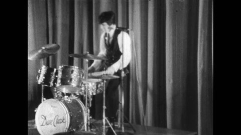 1960s: Man plays drums while on stage. Woman in crowd screams. Women in crowd dance. Woman in crowd gyrates her head.