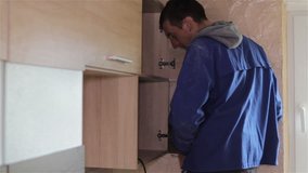 Young man assembling kitchen furniture,Repairman In Overalls Repairing Cabinet Hinge In Kitchen