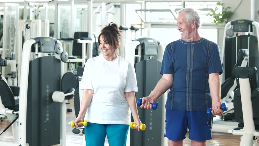 Elderly couple working out at gym. Happy senior man and woman lifting dumbbells at gym. Beautiful elderly people at fitness club.