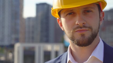 young attractive man in a yellow hard hat looks into the camera. Portrait of a handsome business man.