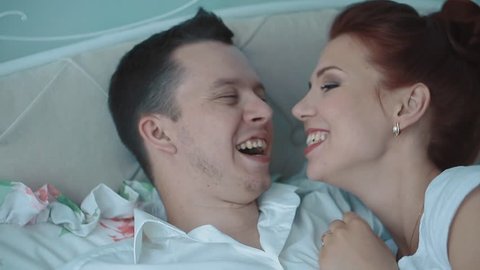 Young beautiful couple resting in bed, laughing, yawning, close-up, slow motion 