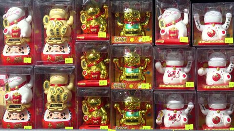 HONG KONG - NOV 2, 2017: Small figures or statues of beckoning or lucky cat with moving upright paws in plastic packaging displayed in shop or store window. Traditional Chinese symbol of good luck.
