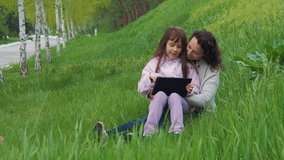 Family in nature with a tablet. Daughter with mother in the park with a tablet.