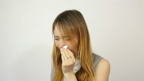Beautiful young woman sneezing into a handkerchief. grey background