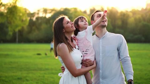 Happy Young Family with child walking on summer field. Healthy mother, father and little daughter girl enjoying nature together, outdoors. Sunset.